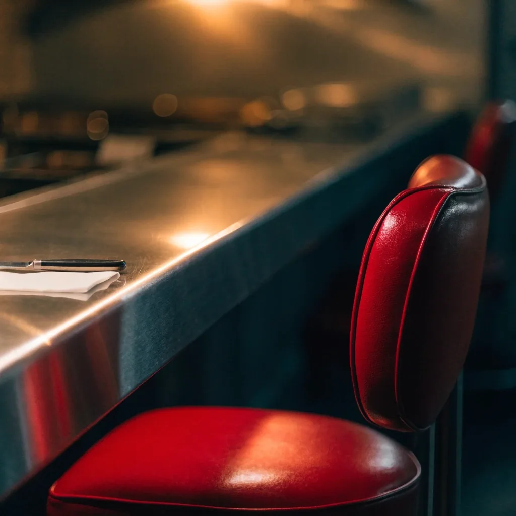Blank paper order tickets clipped on a stainless rail above a diner pass, amber lamp light